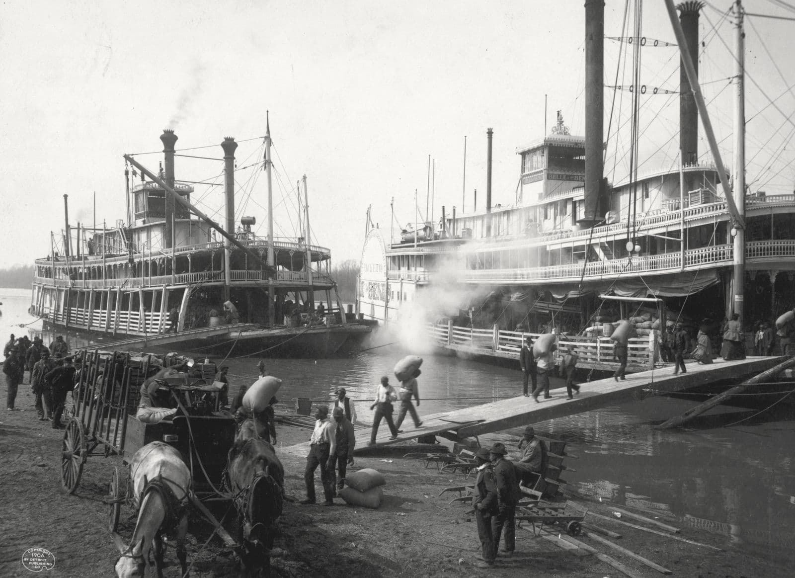 Two Mississippi steamboats at a levee, roustabouts carrying sacks up a gangplank, a horse cart in the foreground; Vicksburg, 1906.