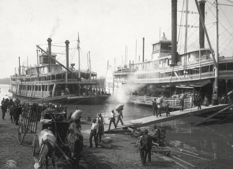 Two Mississippi steamboats at a levee, roustabouts carrying sacks up a gangplank, a horse cart in the foreground; Vicksburg, 1906.