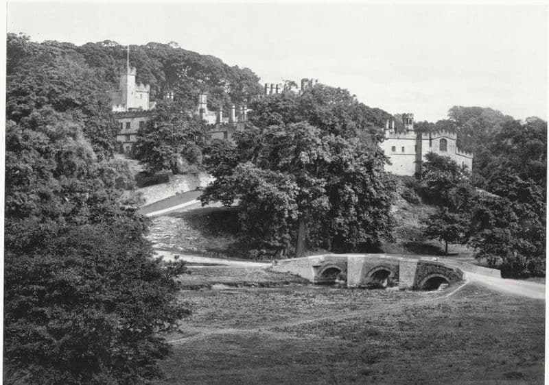 Haddon Hall on its wooded rise above a three-arch packhorse bridge.